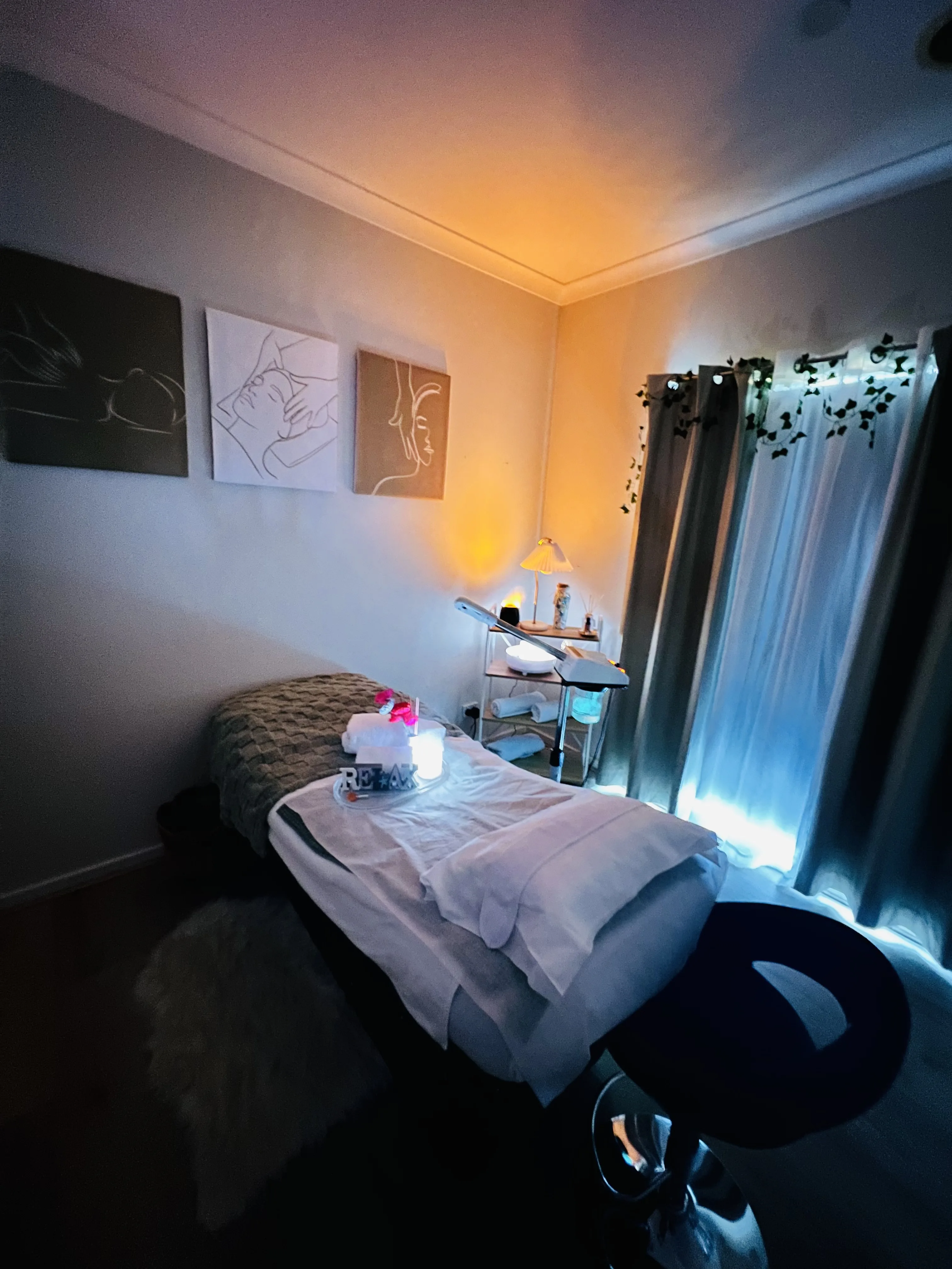 The My Beauty Stop facial treatment room — a draped bed with a RELAX sign, single-line face artworks on the wall, a skin-analysis magnifier, and fairy-lit curtains