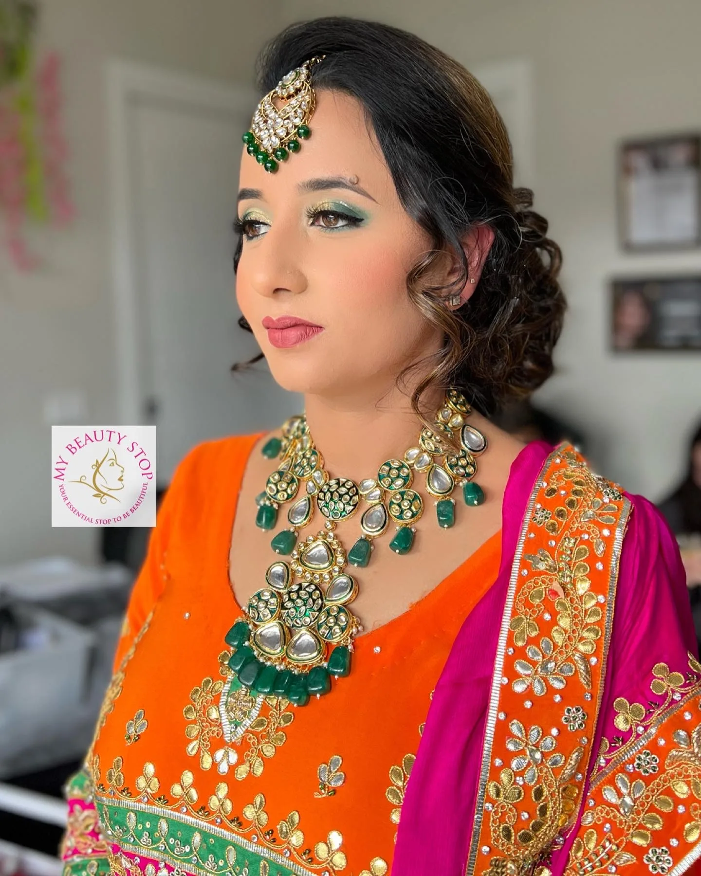 Bridal makeup client in orange-pink Indian wear — green smokey eye, maang-tikka, kundan jewellery